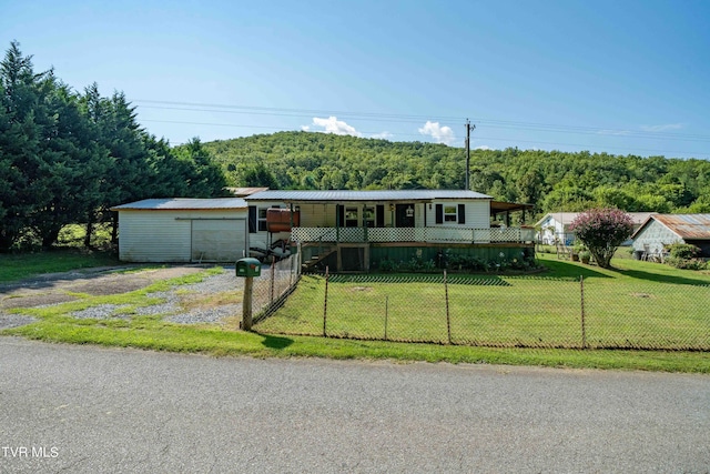 manufactured / mobile home with metal roof, a front lawn, a wooded view, driveway, and fence