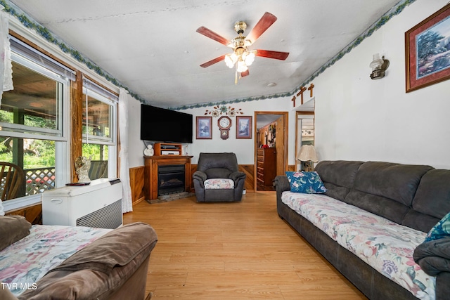 living area featuring light wood finished floors, wainscoting, lofted ceiling, a ceiling fan, and a fireplace