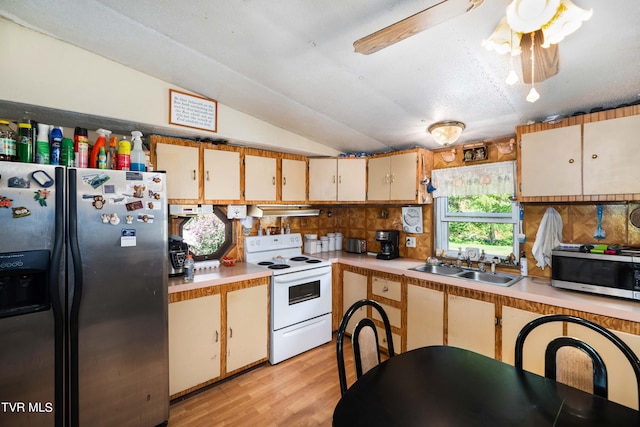 kitchen featuring appliances with stainless steel finishes, light countertops, a sink, lofted ceiling, and light wood-style floors