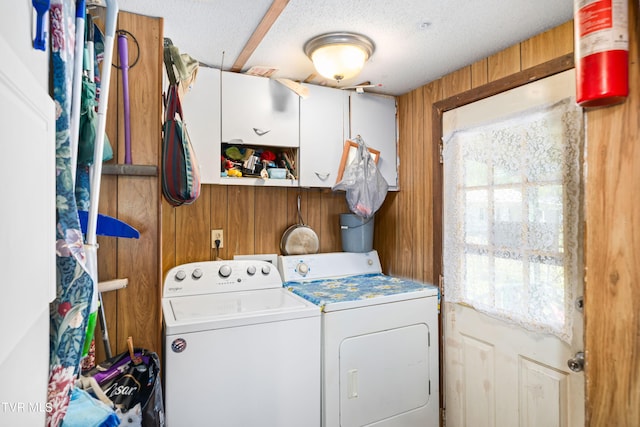 laundry area featuring a healthy amount of sunlight, wooden walls, washing machine and clothes dryer, cabinet space, and a textured ceiling