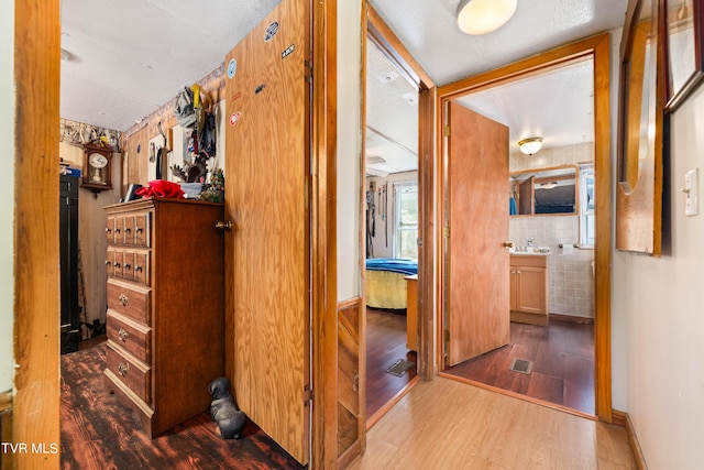 hallway with baseboards, visible vents, a sink, and wood finished floors