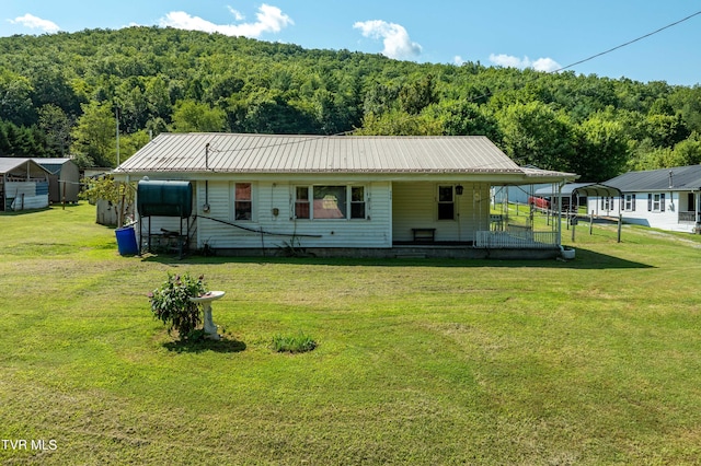 view of front of house with metal roof, a front yard, a detached carport, and a view of trees