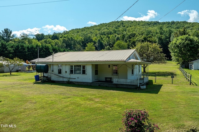 view of front of home featuring metal roof, fence, a front lawn, and a wooded view