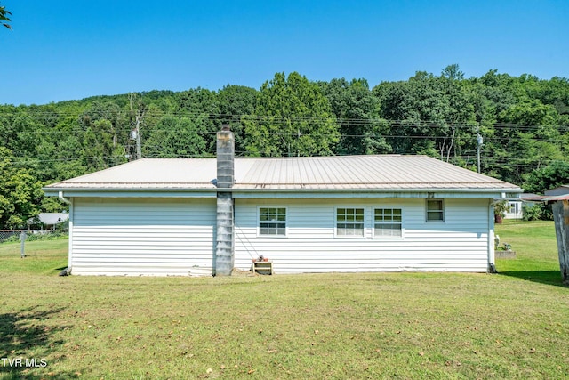 view of property exterior featuring metal roof, a forest view, a lawn, and a chimney