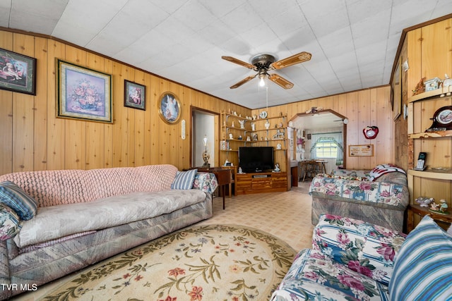 living room with a ceiling fan, light carpet, arched walkways, and wooden walls