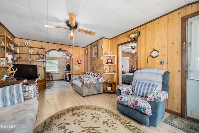 living area featuring crown molding, ceiling fan, and wood walls