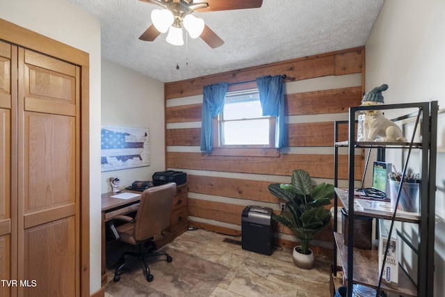 office area featuring a ceiling fan, wood walls, and a textured ceiling