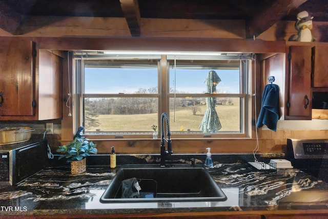 kitchen with a wealth of natural light, dark countertops, stainless steel microwave, and a sink