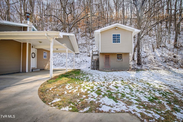 view of snowy exterior featuring an attached carport, driveway, and stairway