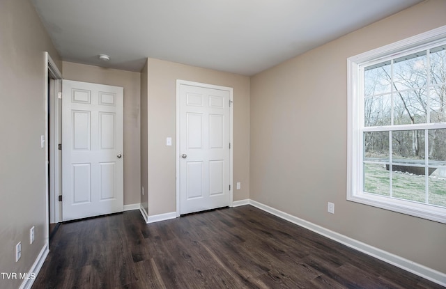 unfurnished bedroom featuring multiple windows, baseboards, and dark wood-style flooring