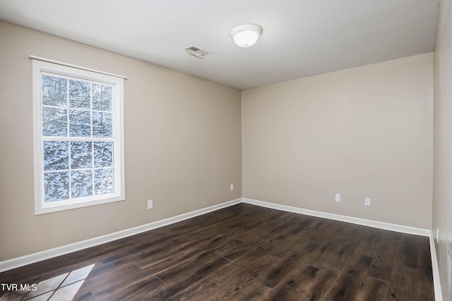 spare room featuring plenty of natural light, dark wood finished floors, visible vents, and baseboards