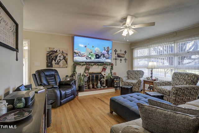 living area with ceiling fan, a glass covered fireplace, crown molding, and wood finished floors