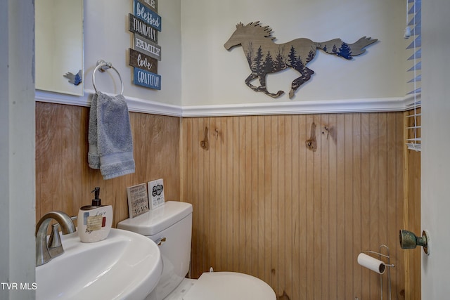 bathroom with toilet, wood walls, a sink, and wainscoting