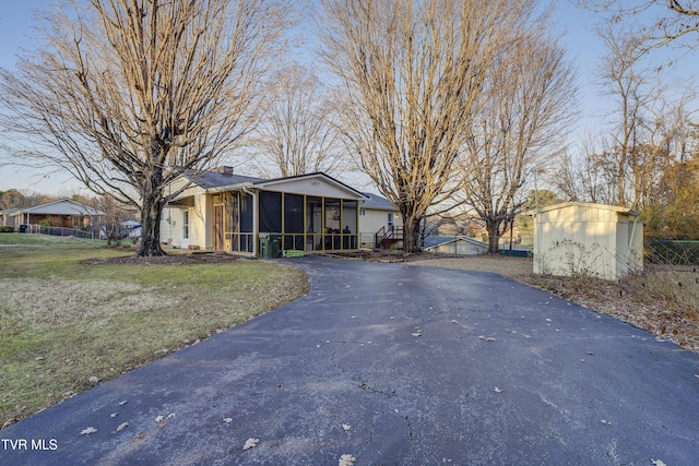 exterior space featuring a chimney, a sunroom, an outdoor structure, driveway, and a front lawn