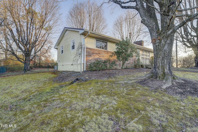 view of property exterior featuring a yard, brick siding, a chimney, and fence