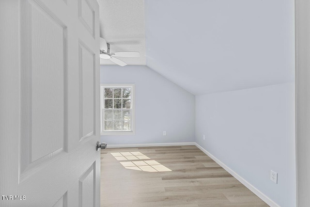 additional living space with lofted ceiling, light wood-style flooring, a ceiling fan, a textured ceiling, and baseboards