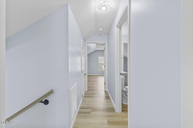 hall with light wood finished floors, lofted ceiling, visible vents, a textured ceiling, and baseboards