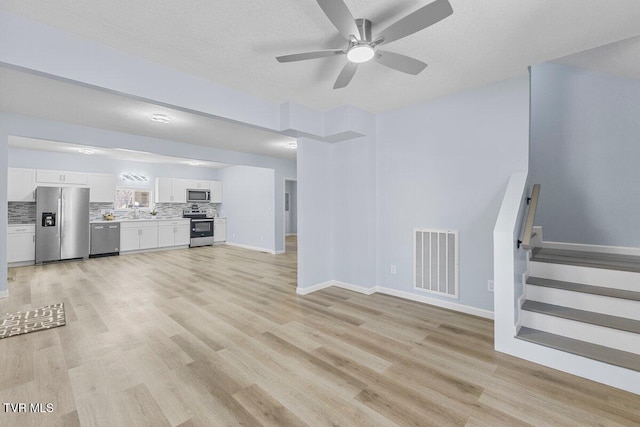 unfurnished living room featuring stairway, a textured ceiling, visible vents, and light wood-style floors