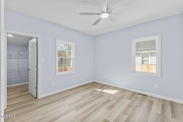 unfurnished bedroom featuring visible vents, baseboards, a spacious closet, a closet, and light wood finished floors