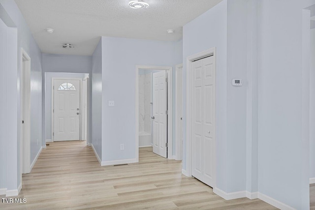 foyer entrance with light wood-style floors, baseboards, and a textured ceiling