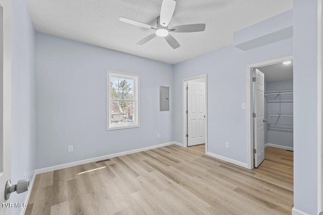 unfurnished bedroom featuring light wood-style flooring, visible vents, baseboards, a spacious closet, and electric panel