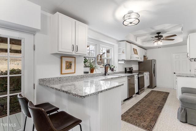 kitchen featuring white cabinets, light stone counters, appliances with stainless steel finishes, a peninsula, and a sink