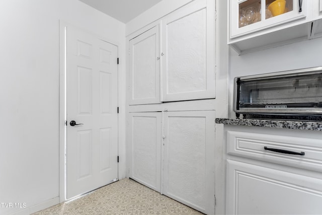 interior space with glass insert cabinets, dark stone counters, a toaster, and white cabinetry