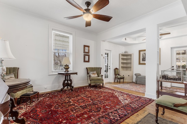 sitting room with a ceiling fan, crown molding, baseboards, and wood finished floors