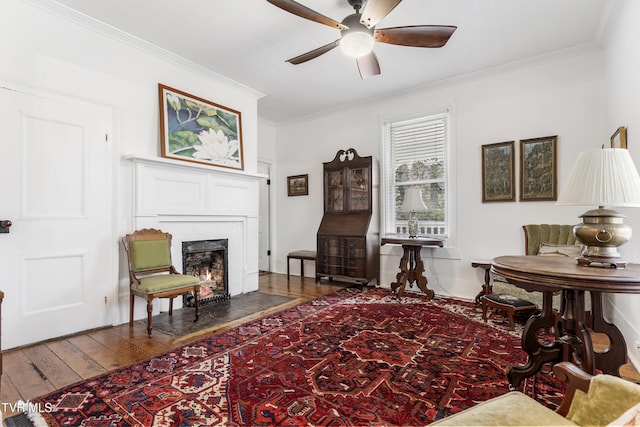 sitting room with a ceiling fan, crown molding, a lit fireplace, and wood finished floors