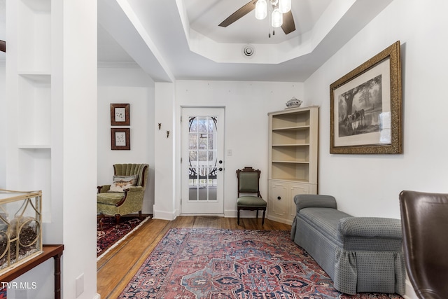 living area with a tray ceiling, ceiling fan, and wood finished floors