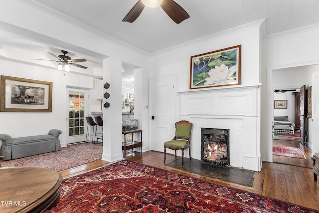 living area with dark wood-type flooring, ornamental molding, and a fireplace with flush hearth