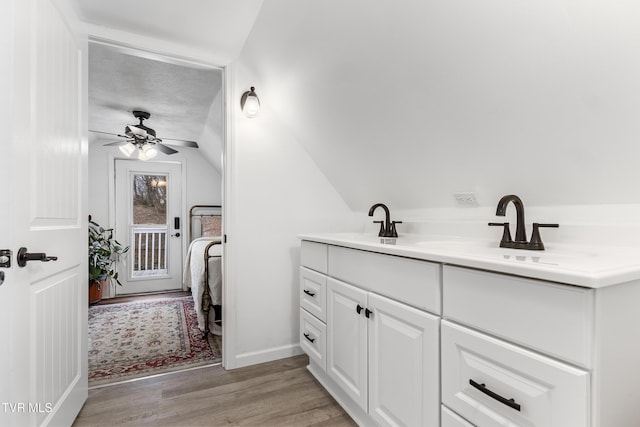 ensuite bathroom featuring baseboards, connected bathroom, wood finished floors, vaulted ceiling, and vanity