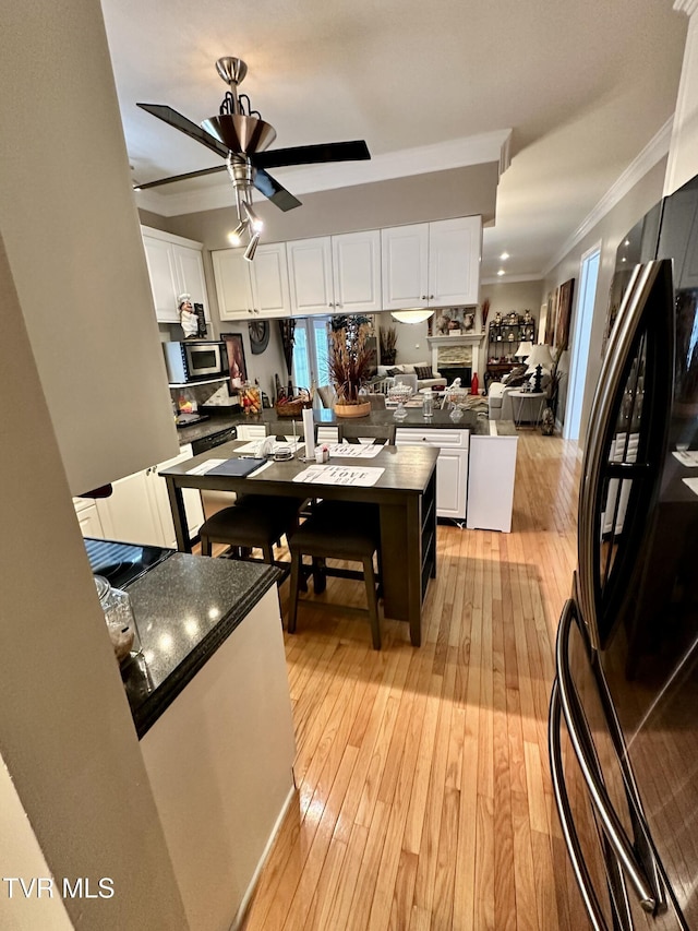 kitchen featuring white cabinets, freestanding refrigerator, stainless steel microwave, dark countertops, and crown molding