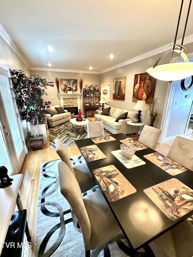 dining space featuring wood-type flooring, a fireplace, ornamental molding, and recessed lighting