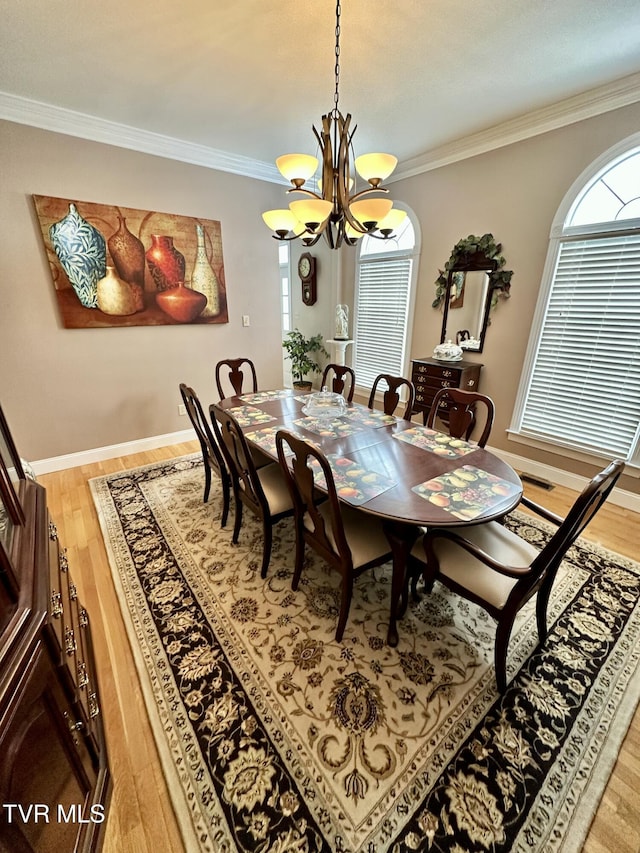 dining area with a healthy amount of sunlight, a notable chandelier, light wood-style flooring, and crown molding