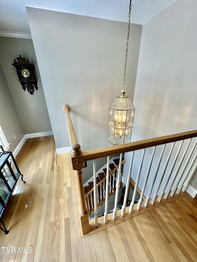 stairs featuring wood-type flooring, crown molding, a chandelier, and baseboards