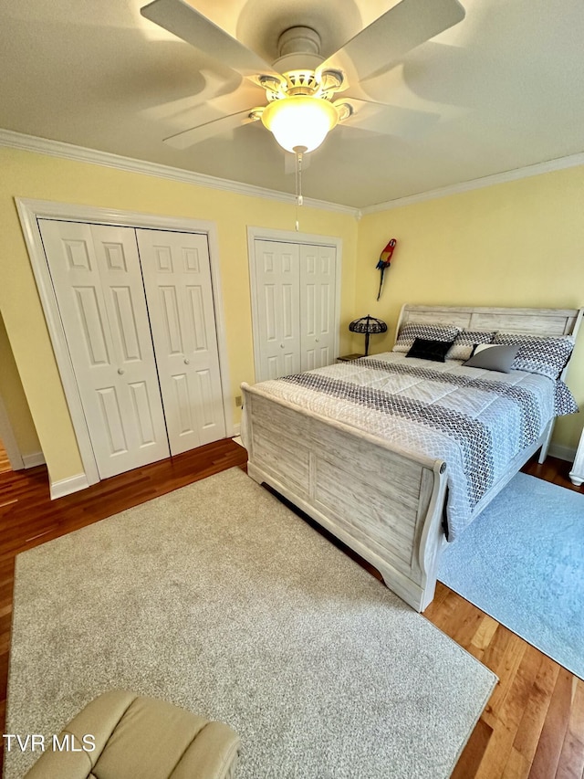 bedroom with crown molding, two closets, ceiling fan, wood finished floors, and baseboards