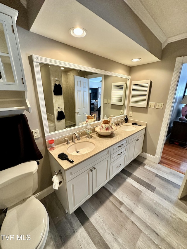 full bathroom with toilet, ornamental molding, a sink, and wood finished floors