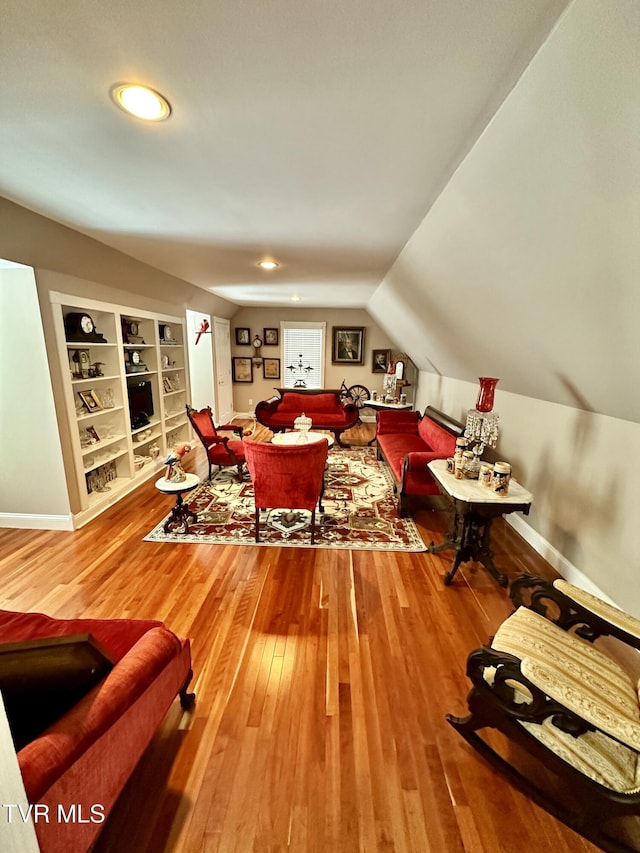 living room with built in shelves, vaulted ceiling, baseboards, and hardwood / wood-style flooring