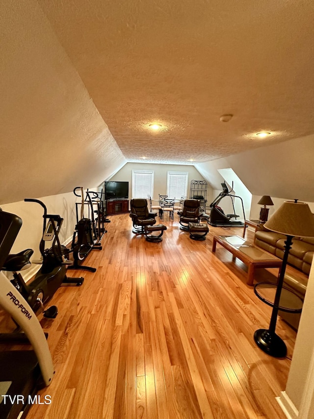 exercise area with vaulted ceiling, a textured ceiling, and hardwood / wood-style floors