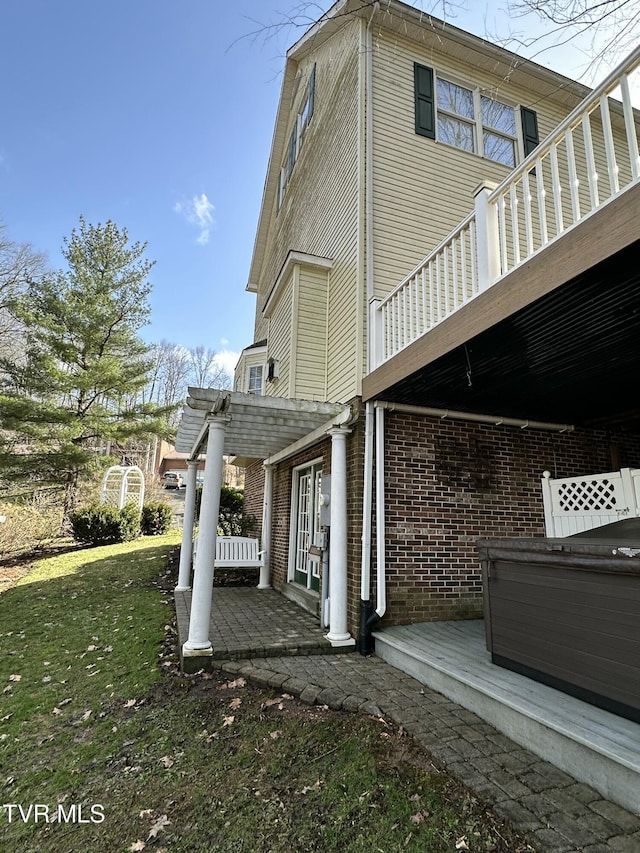 view of side of home featuring brick siding, a patio, a lawn, a hot tub, and a pergola