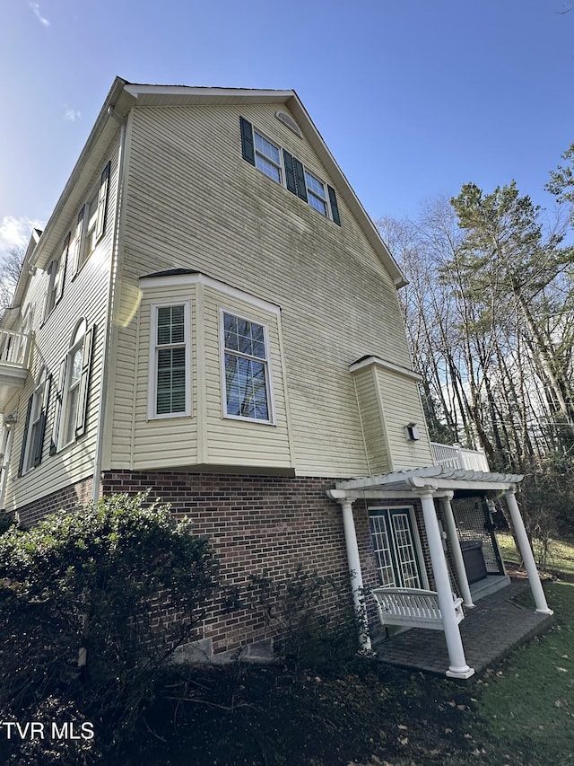 view of side of home featuring brick siding and a pergola