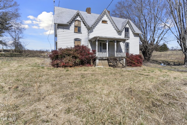 victorian house with a front yard, covered porch, and a chimney