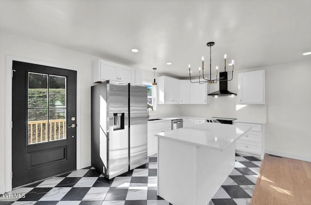 kitchen featuring light countertops, appliances with stainless steel finishes, white cabinetry, a kitchen island, and wall chimney exhaust hood