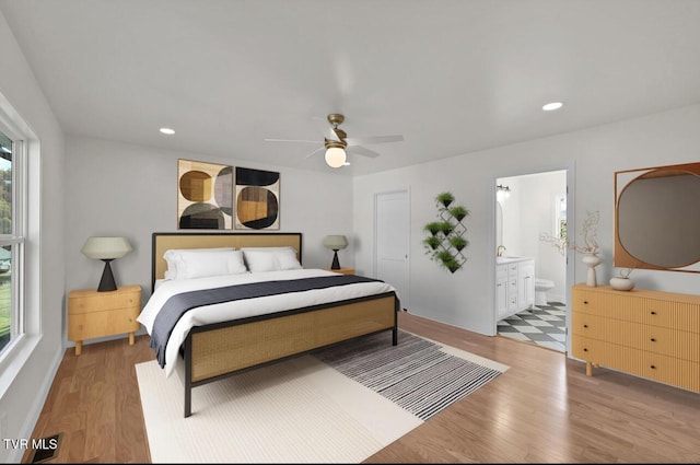 bedroom featuring ceiling fan, light wood-style flooring, ensuite bathroom, a sink, and recessed lighting