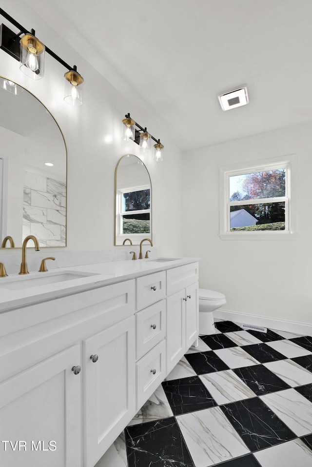 bathroom with marble finish floor, double vanity, a sink, and toilet