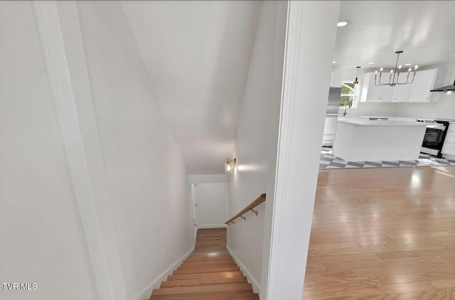 stairway with baseboards, a chandelier, and wood finished floors