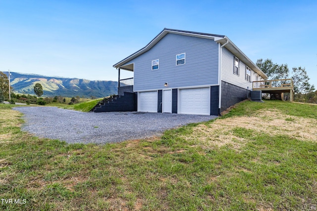 view of property exterior with a garage, driveway, central AC unit, a lawn, and a deck with mountain view