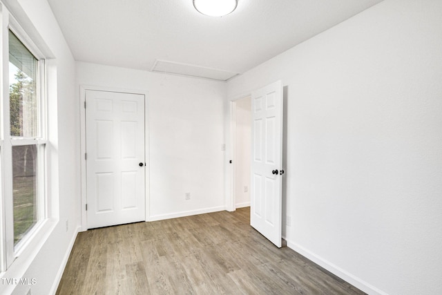 unfurnished bedroom with light wood-style floors, attic access, and baseboards