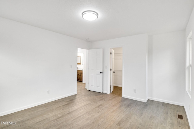 unfurnished bedroom with baseboards, visible vents, a spacious closet, and light wood finished floors